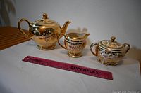 Photo showing teapot, creamer, and sugar bowl arranged with a ruler for size reference on a white surface.