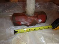 Close-up of red metal sledgehammer head and tape measure showing about 7 inch width of striking face.