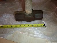 Sledgehammer head with measuring tape showing length approx 9 inches
