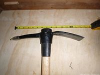 Close-up of the black metal mattock/pick head with a measuring tape extended showing approximately 10 inches across the head.