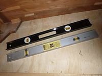 Two Stanley 24 inch metal levels on a wooden surface, black level on top and grey level below.