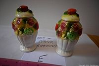 Pair of ceramic salt and pepper shakers designed as strawberry and fruit bouquets with colorful hand-painted detail, white base and red strawberry tops, photographed with a ruler for scale.