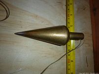 Side view of vintage brass plumb bob with removable pointed tip, showing size against measuring tape.