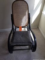 Front view of the black bent wood rocking chair with woven cane backrest and seat, showing a cushion on the seat.