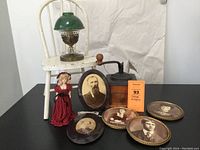 Five framed ancestor photographs, white chair, green glass oil lamp, coffee grinder and doll displayed on black table