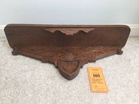 Full view of decorative wooden wall shelf laying flat showing front decorative carved details and hooks.