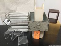 Lot showing all items including two-tier metal vanity organizer with glass shelves, three acrylic plexiglass risers, large distressed metal box with ring pull, two wooden display boxes, and small white stool.