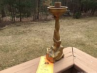 Antique figural lamp displayed outdoors on a wooden deck, showing the lamp base with the female figure and the socket for the bulb on top.