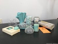 Full shot showing all decorative items including ceramic vase, glass sea urchins, candles, stones, pebbles, and container of small pebbles on black surface.