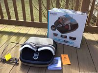 Photo of the Homedics Shiatsu AirMax foot massager alongside its original box, power cord, and manual, displayed outdoors on a wooden deck.