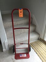 Front view of red metal two-wheeled dolly with rectangular platform and tall handle.