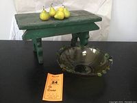 Green wooden bench with six yellow plastic pears on top and glass bowl next to it