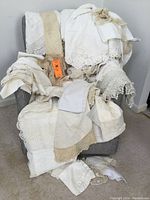 Full view of lot showing various vintage fabric pieces in linen and lace draped over chair, including tablecloths, doilies, bed skirt and runners with visible lace trims and crochet lace