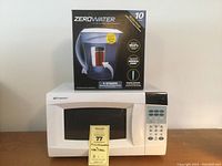 Front view of the Emerson mini microwave on a wooden surface with the ZeroWater 10-cup filter pitcher box placed on top.