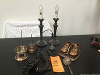Photo showing all lot items together: bronzed baby shoe bookends, two lamps, cast iron sconce, message spike, oil cans, and strainer spoon.