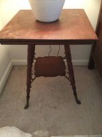 Oak square table with turned legs shown from front with lower scalloped shelf. Tabletop surface finish damaged with visible stains and wear.