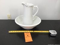 White ceramic pitcher placed inside a white bowl, taped measure placed to show pitcher height around 12 in