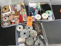 Three plastic storage boxes filled with a variety of crafting ribbons and bits including fabric trims, ribbons, and embellishments in different colors and styles.