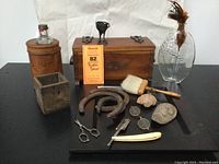 Full lot view showing wooden boxes, horseshoes, razor, spectacles, wooden tray, glass grape vase with feather, stone faces, and ink bottle.
