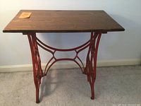 Front view of wooden top table mounted on red metal Eldridge sewing machine base.