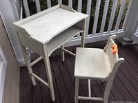 Small off-white painted desk with raised guardrails and open shelf viewed from side angle