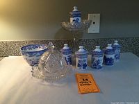 Group view of seven Spode Blue Room Collection spice jars with blue floral and herb patterns and two clear EAPG glassware items including a cheese dome and compote.