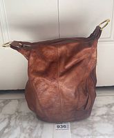 Front view of the brown leather handbag showing the body and gold metal rings on top.