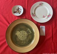Three vintage plates on red cloth: a small square horse head dish, a large round bird plate, and a floral dinner plate