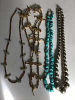 Photo showing four distinct American Indian necklaces laid out flat: two metallic animal motif necklaces, one turquoise bead necklace, and one necklace with white bird beads alternating with small brown beads.