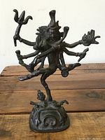 Front clear view of the multi-armed metal figure statue, showing detailed arms and facial features, standing posed on a base with an additional small figure.