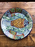 Top view of ceramic plate with colorful fish and leaf pattern on wooden surface.