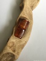 Photo of amber-colored cheroot holder resting on a carved wooden surface, showing side view and amber translucency.