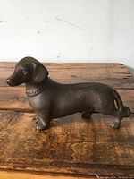 Side view of the solid cast iron dachshund dog figurine on a wooden surface showing textured surface and collar detail.