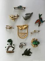 Top view of assorted animal brooches laid out on white surface showing dolphins, birds, frog, turtle, cow, and other designs.