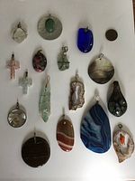 All pendants laid out on white surface with a penny for scale, showing variety in shapes, colors and styles.