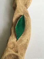 Top view of a mid-century modern leaf-shaped brooch with bright green guilloche enamel and sterling silver frame on a wooden surface.