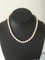 Full view of natural pearl necklace displayed on black bust to show overall length and pearl size.