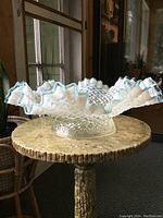 Side angled view of the scalloped ruffled edge and hobnail diamond pattern on the opalescent glass bowl, showing the translucent white with bluish edge tint.