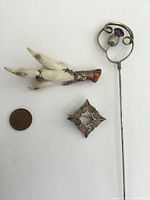 Top view showing all three Scottish jewelry items including the long silver thistle pin, grouse foot pin with fur detail, and geometric metal brooch alongside a coin for scale.