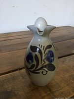 Front view of small antique pottery syrup jug showing floral decoration and bulbed lid