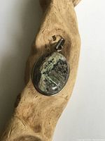 Oval sterling silver pendant with large polished green-black-white agate boulder, viewed from front on wooden display