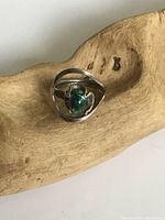 Front angle view of sterling silver modernist ring with multicolored opal center on wooden display.