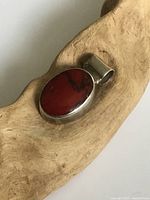 Close-up of oval red stone set in sterling silver pendant resting on a light tan wood surface.