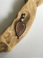 Front view of the sterling silver pendant with rose quartz stone and pearl on a wooden surface.