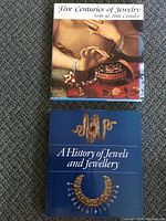 Two hardcover jewelry coffee table books placed on carpet, the titles visible: 'Five Centuries of Jewelry 16th to 20th Century' and 'A History of Jewels and Jewellery'.