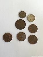 Seven assorted coins of various sizes, colors, and designs laid out on a white background showing obverse and reverse sides with visible wear.