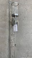 Full view of acrylic wall sconce mounted on a concrete wall, showing cylindrical frosted shade with silver trim, clear acrylic rod extending downward, and round silver mounting plate.
