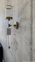 Side profile photo of acrylic wall sconce mounted on a concrete wall showing gold metal mount, clear acrylic shade, and pull chain detail.