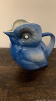 Side view of blue bird-shaped porcelain pitcher showing detailed bird features in blue glaze.