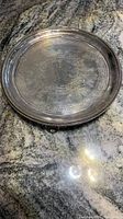 Full view of round antique silver plated footed tray on granite surface, showing overall condition and shape.